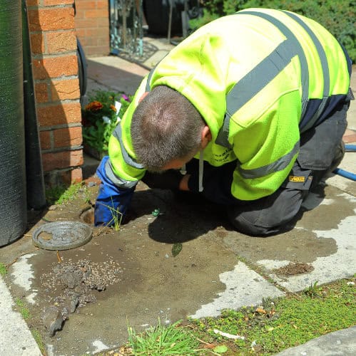A drain engineer with his arm down a blocked drain clearing part of a blockage