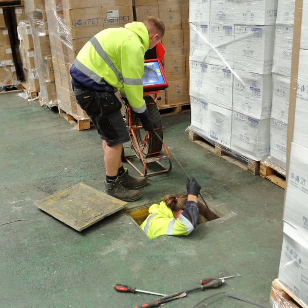 Two drain experts working in a warehouse clearing a blocked drain
