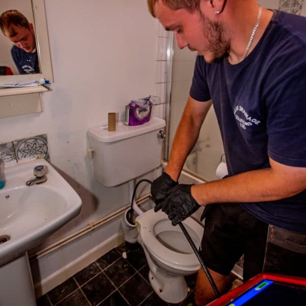A drain engineer unblocking a toilet in a house bathroom